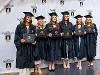 Graduates in caps and gowns smiling, holding their degrees.