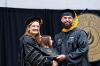 Acting President Dr. Shonna Riedlinger shakes hands with a graduate while handing him a degree.