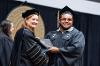 Acting President Dr. Shonna Riedlinger shakes hands with a graduate while handing him a degree.